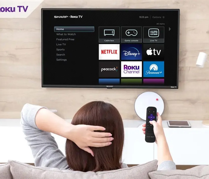 Woman relaxing on couch while pointing remote control at a Sharp Roku tv.